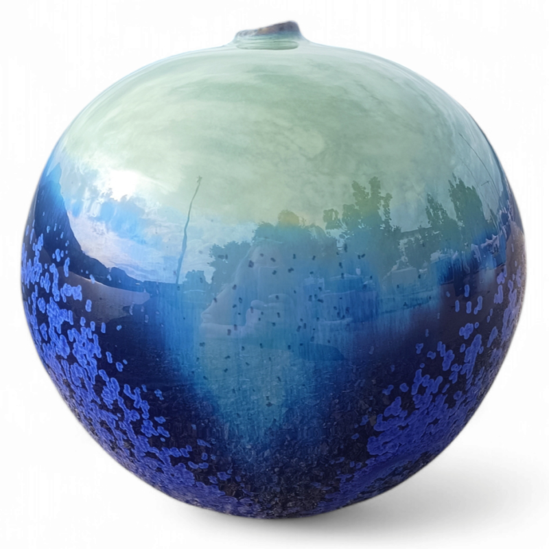 Een ronde keramische bol met een glanzende afwerking, waarbij de kleuren verlopen van lichtgroen bovenaan naar diepblauw onderaan, met een gespikkeld patroon en reflecties van de omgeving zichtbaar op het oppervlak.